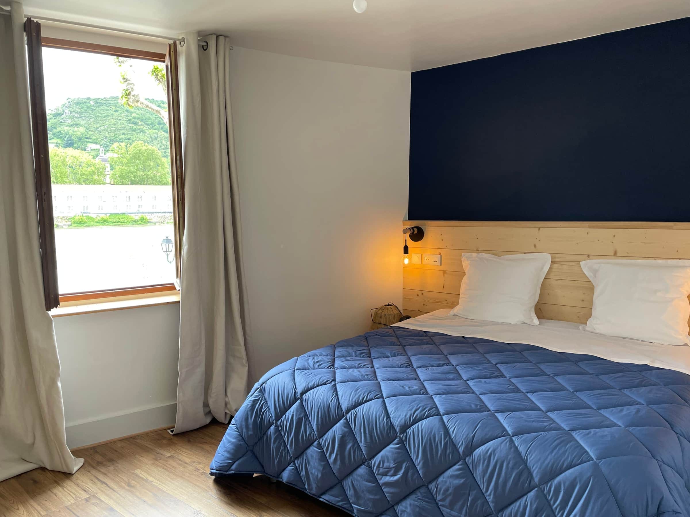 Chambre du premier étage avec lit king size, mur bleu nuit et fenêtre ouverte sur le Rhône et les coteaux